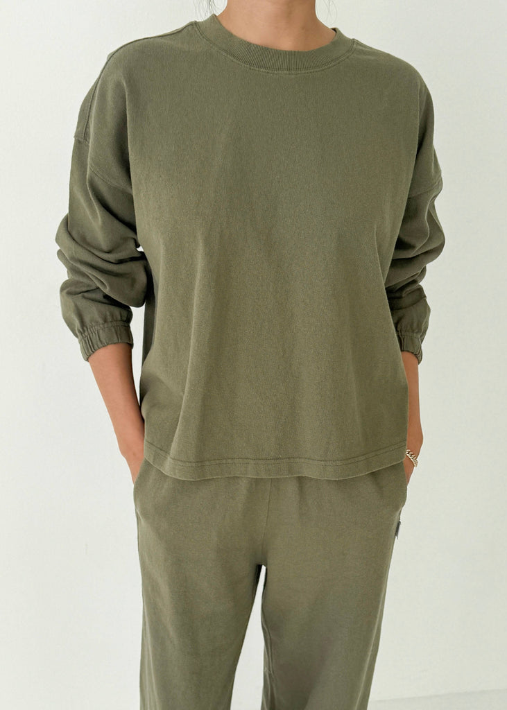 Person wearing an olive green sweatshirt and pants on a white background