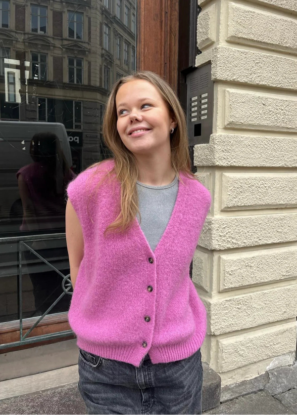 Person wearing a pink cardigan standing outside a building.
