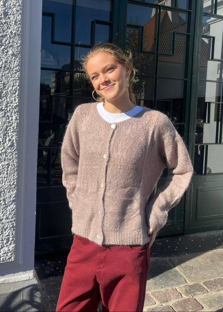 Woman wearing a beige cardigan and red pants standing outside a building with reflective glass windows.