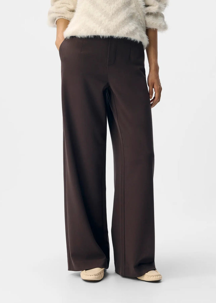 Brown wide-leg pants worn with a light-colored sweater on a white background