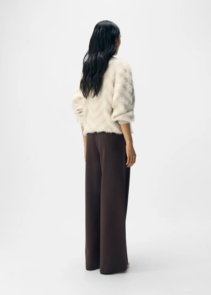 Person wearing a cream sweater and dark pants on a white background