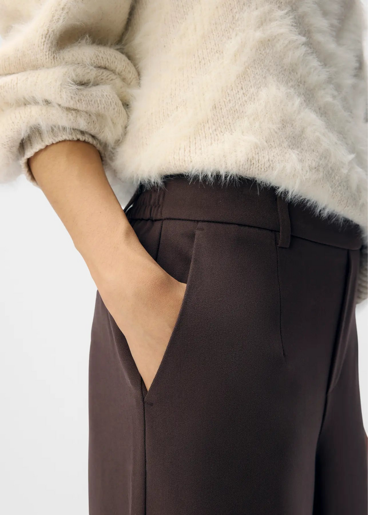 Person wearing a white fluffy sweater and brown pants on a light gray background