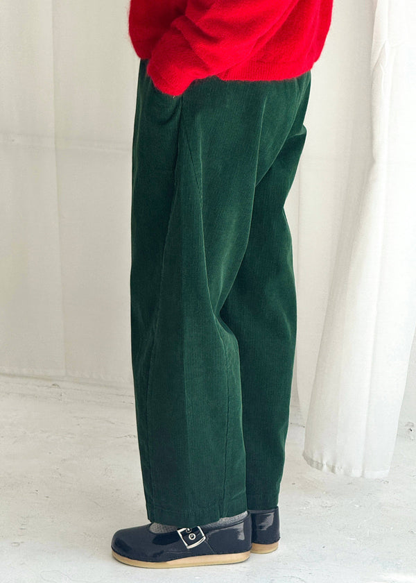Person wearing green pants and a red top against a white curtain background