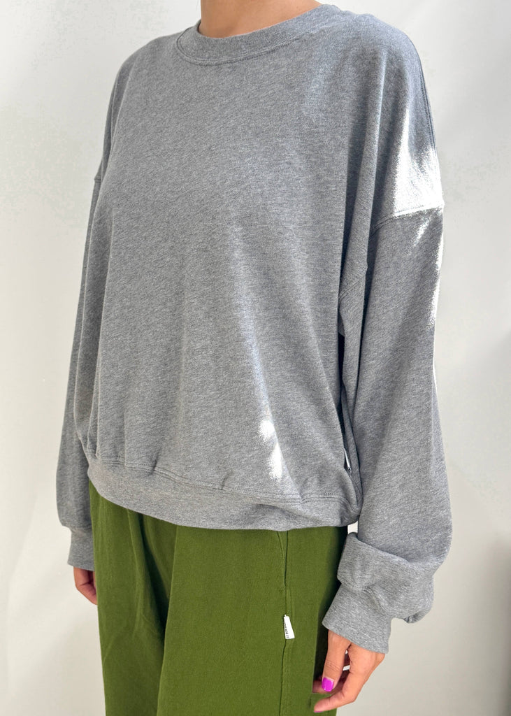 Person wearing a gray sweatshirt and green pants on a plain background