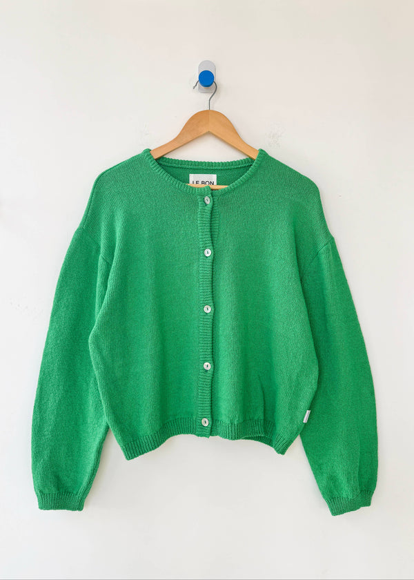 Green cardigan on a wooden hanger against a white background