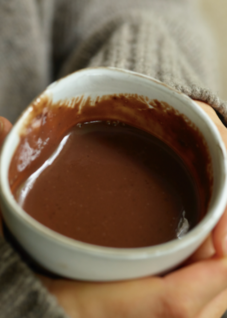 Person holding a small white bowl filled with a brown liquid, possibly hot chocolate.