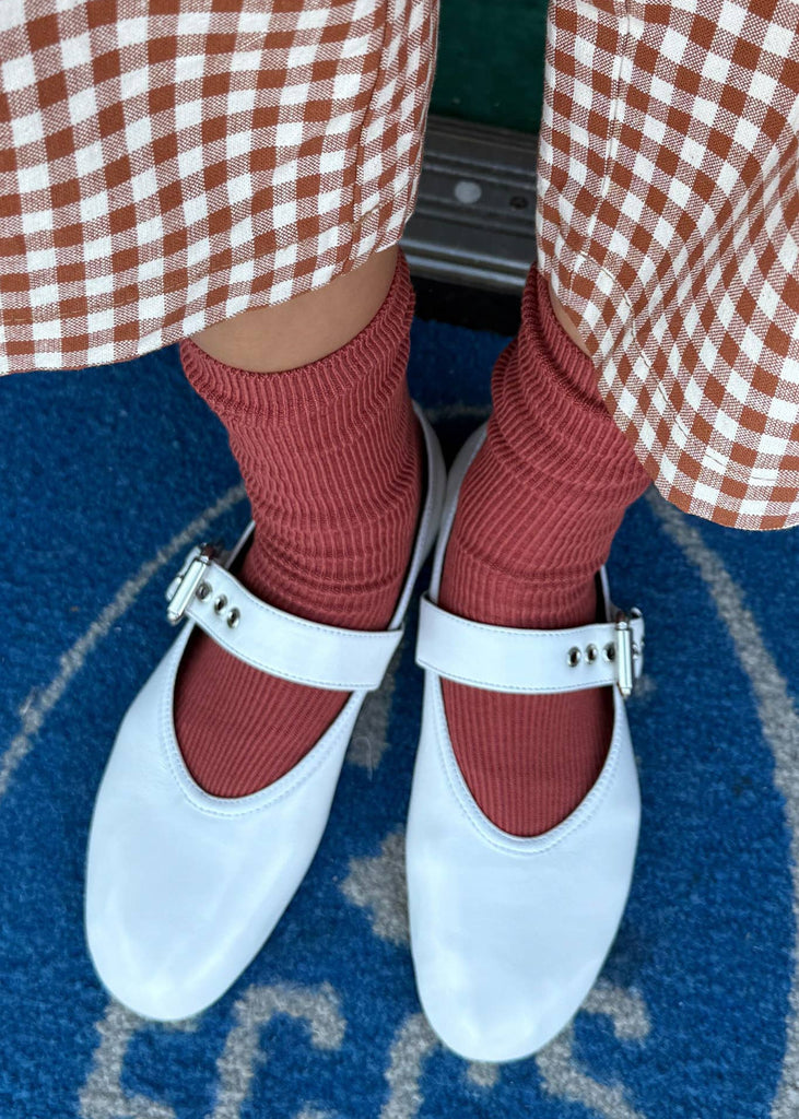 White shoes with buckles worn with red checkered pants and socks on a blue carpet.