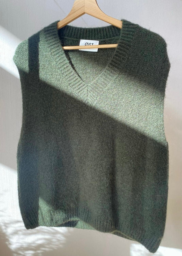 Green knitted sweater on a hanger against a white background
