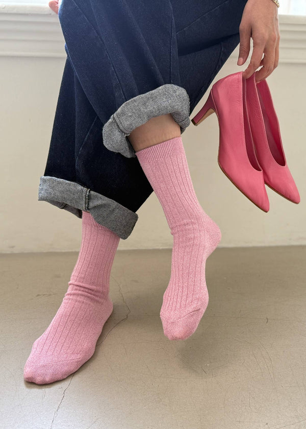 Person wearing pink socks and holding pink high heels on a neutral background