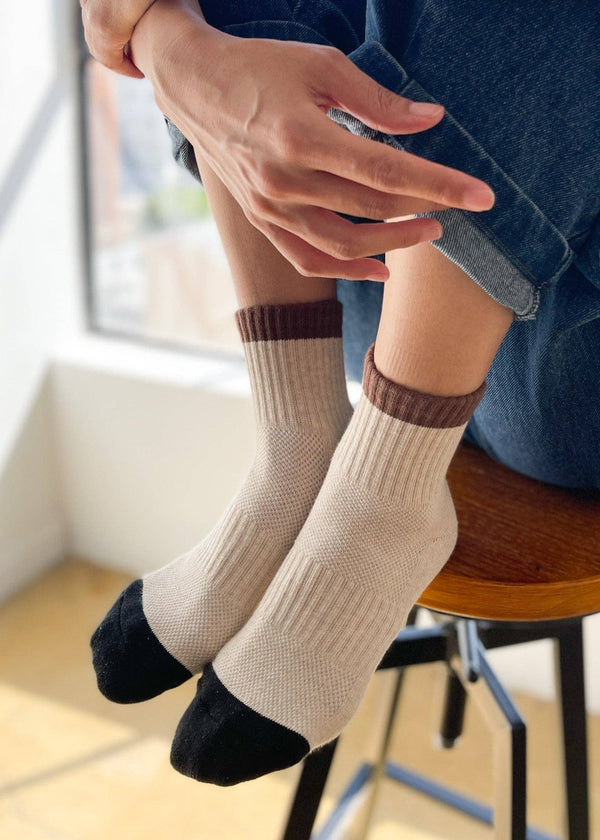 Person wearing beige socks with brown accents sitting on a chair.