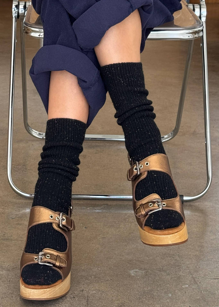 Person wearing black knee-high socks and gold sandals sitting on a chair.
