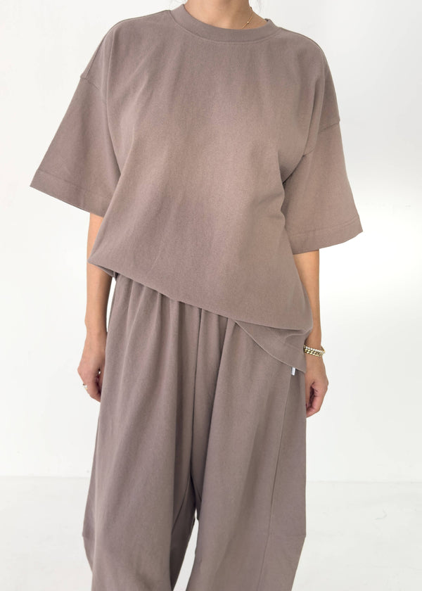 Person wearing a brown oversized t-shirt and pants on a white background