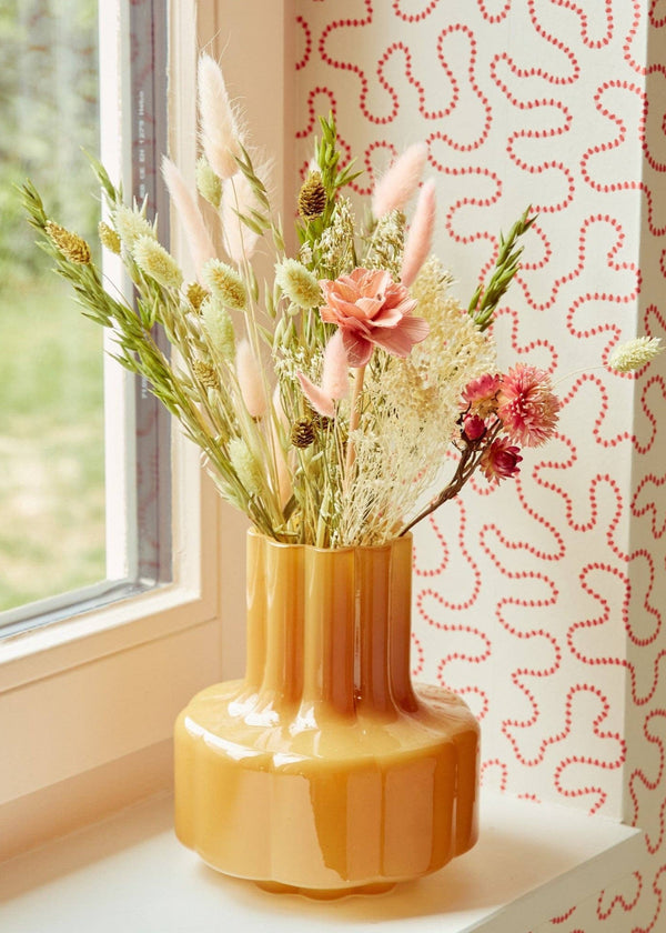 Yellow vase with dried flowers on a windowsill with a patterned wall in the background