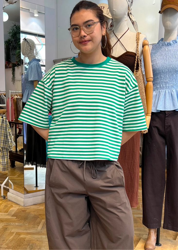 Person wearing a green and white striped shirt and brown pants standing in a clothing store.