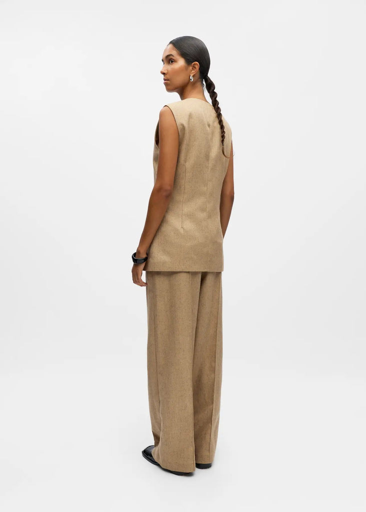 Woman wearing a beige sleeveless top and pants on a white background
