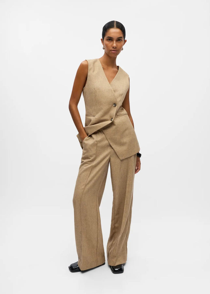 Woman wearing a beige sleeveless top and pants on a white background