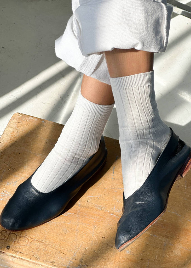 Person wearing navy loafers and white socks on a wooden floor.