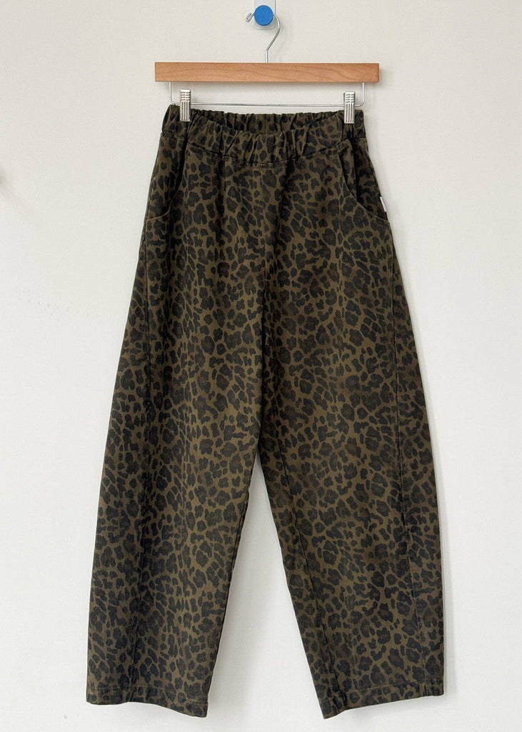 Leopard print pants hanging on a wooden hanger against a white background