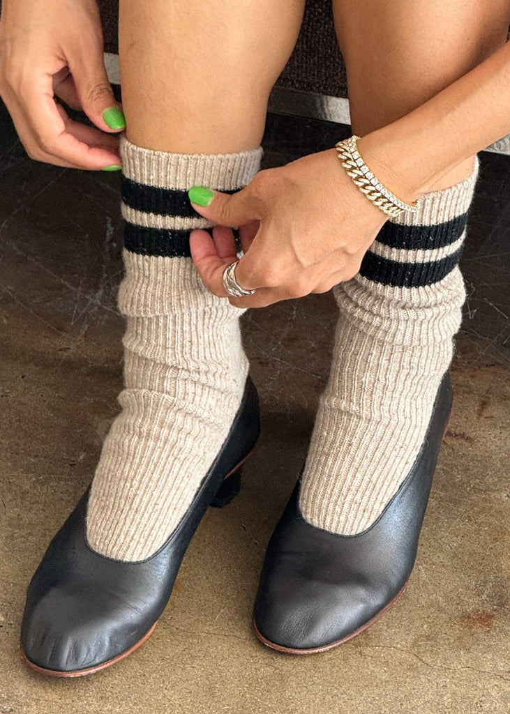 Person wearing beige socks with black stripes and black shoes on a neutral background
