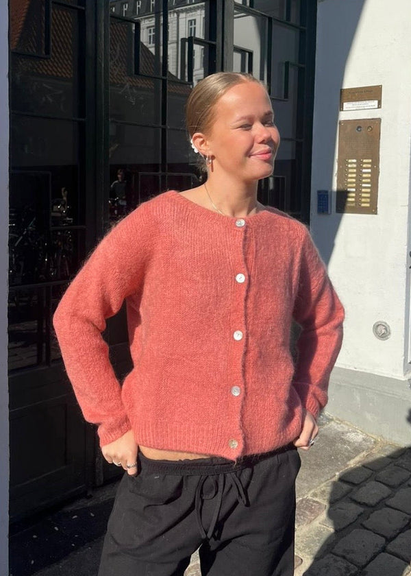 Person wearing a pink cardigan standing on a street.