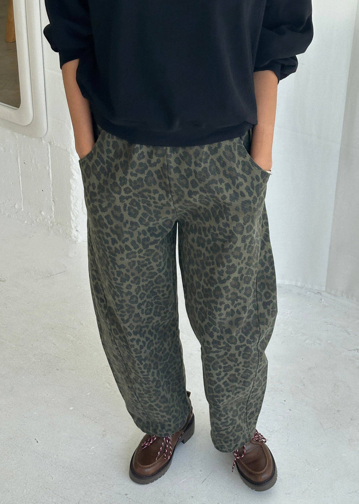 Person wearing leopard print pants and a black top in a minimal indoor setting