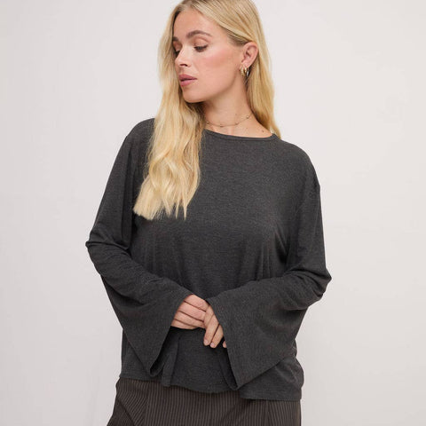 Woman wearing a dark gray long-sleeve top and pants on a light gray background