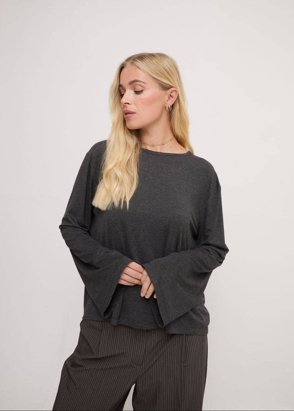 Woman wearing a dark gray long-sleeve top and pants on a light gray background