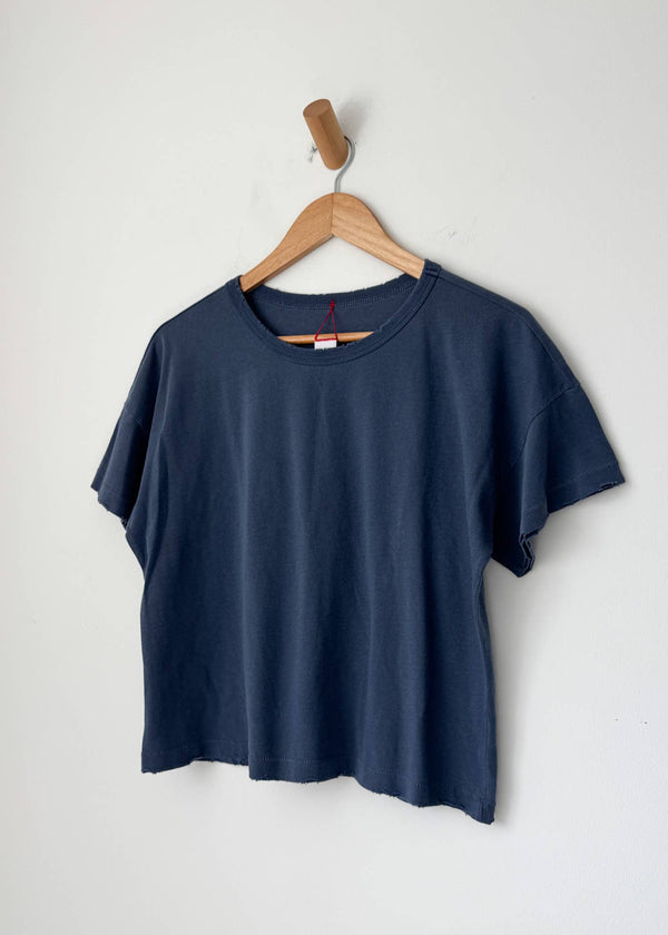 Navy blue t-shirt hanging on a wooden hanger against a white wall