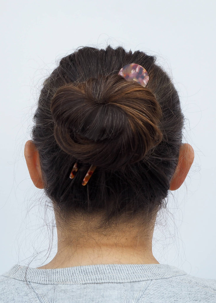 Back view of a person with a bun and decorative hair clip on a light gray background