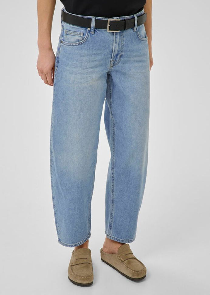 Person wearing light blue jeans and brown shoes on a plain background