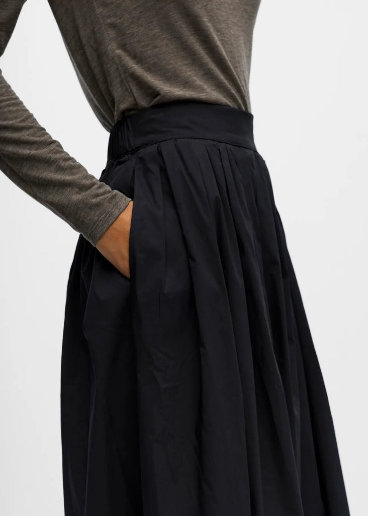Person wearing a black skirt and brown long-sleeve top on a light gray background
