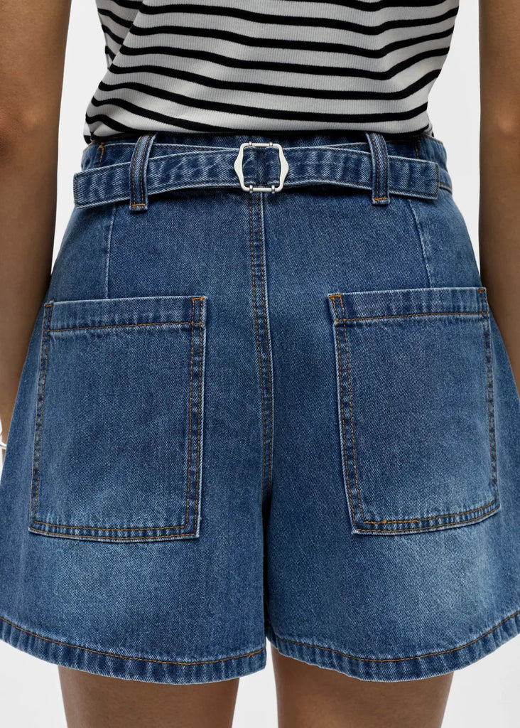 Person wearing blue denim shorts with a striped top on a plain background