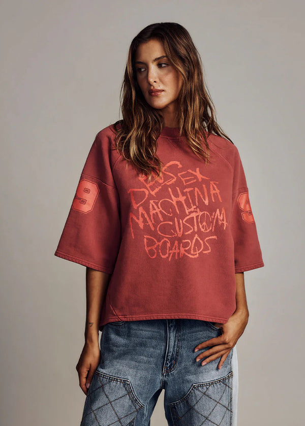 Person wearing a red oversized t-shirt with text on a plain background