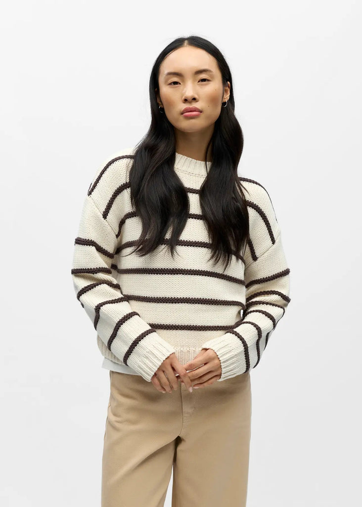 Woman wearing a striped sweater and beige pants against a white background