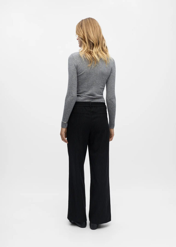 Woman wearing a gray long-sleeve top and black pants on a white background