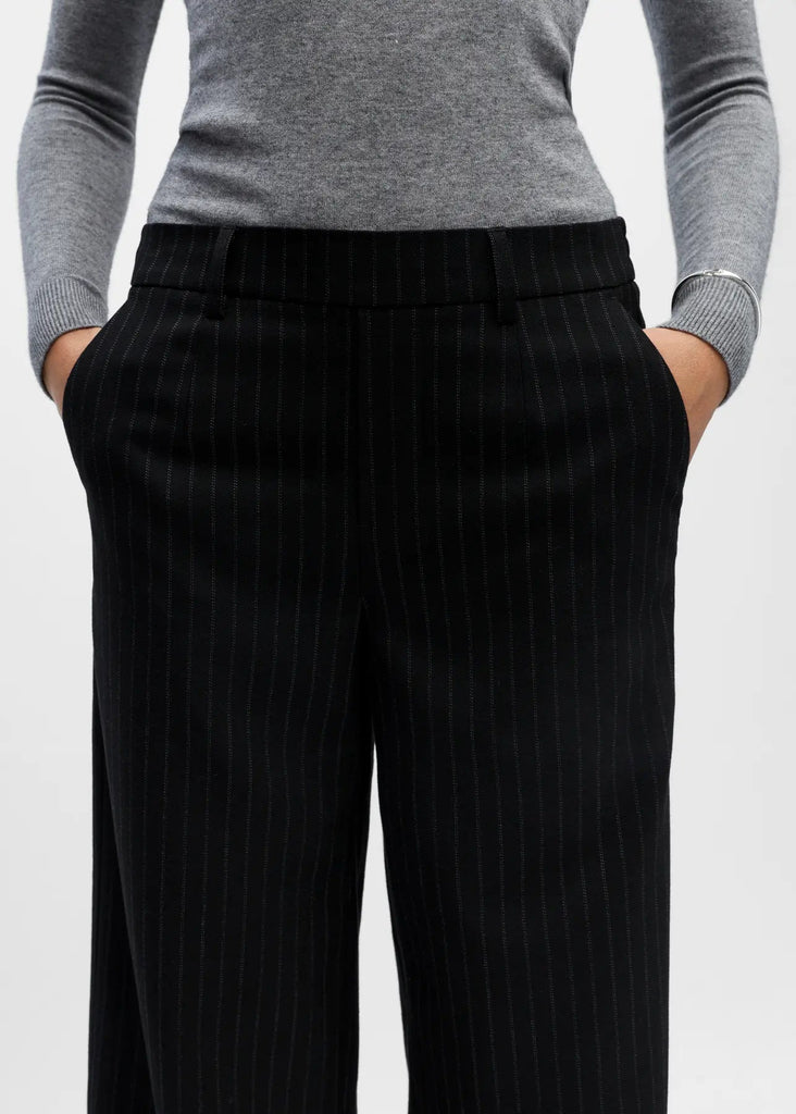 Person wearing black pinstripe pants and a gray sweater on a light gray background