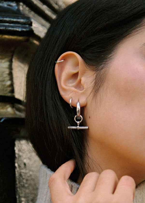 Close-up of a woman's ear with silver hoop earrings against a blurred background
