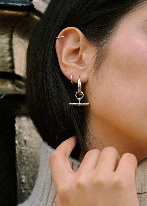 Close-up of a woman wearing a silver earring with a small pendant.