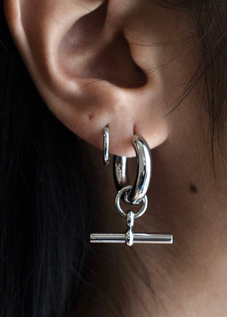 Close-up of an ear wearing a silver hoop earring with a bar pendant.