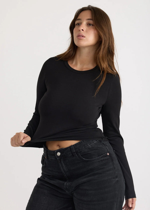 Woman wearing a black long-sleeve top and black jeans on a white background